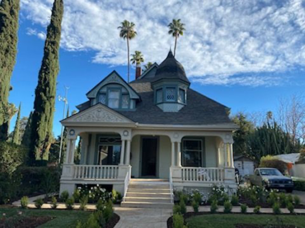 A restored Queen Anne Victorian with a corner turret and wraparound porch under a clear blue sky.