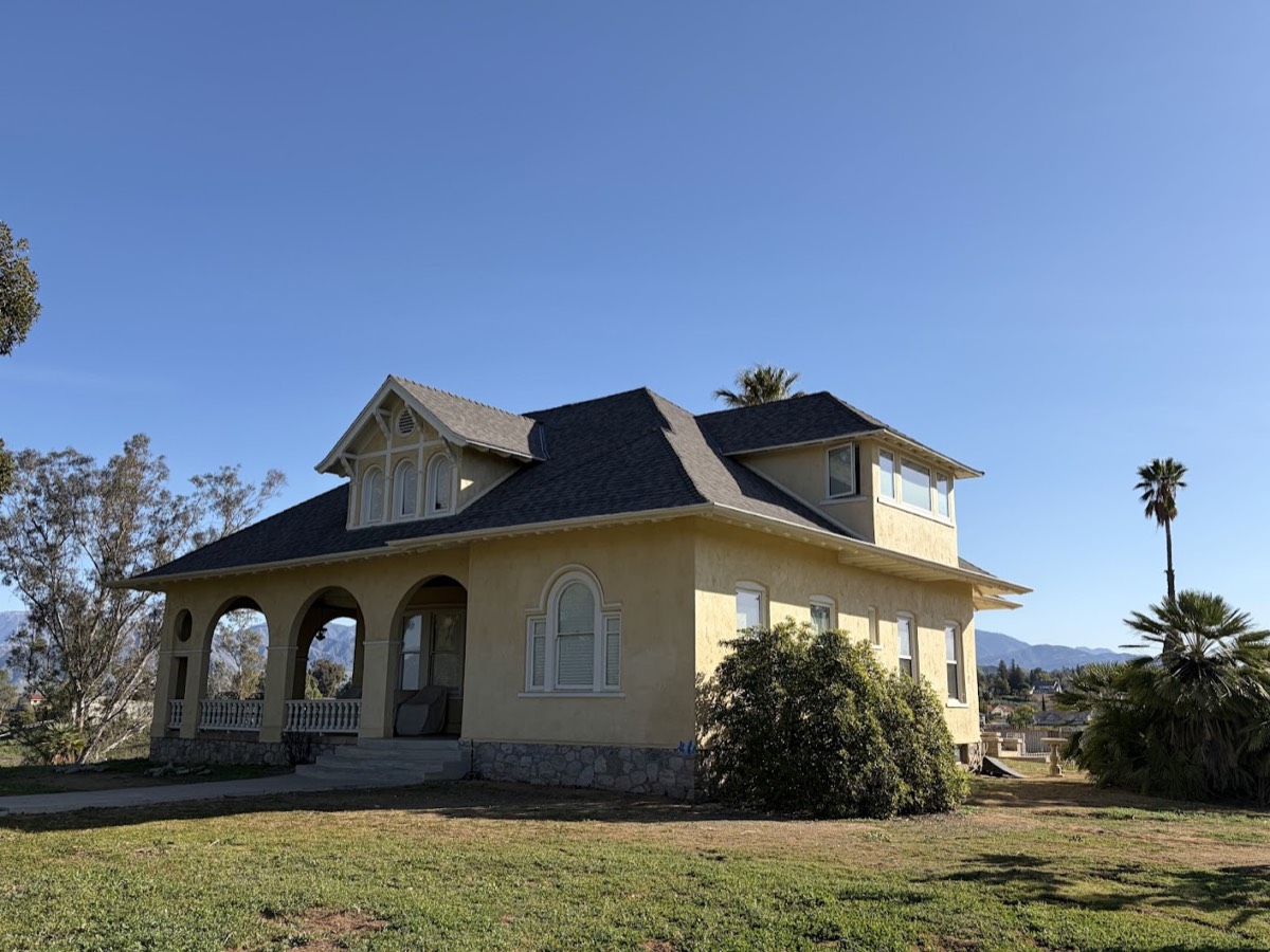 A yellow turn-of-the-century house with a hipped roof and covered porch, mountains in the distance.