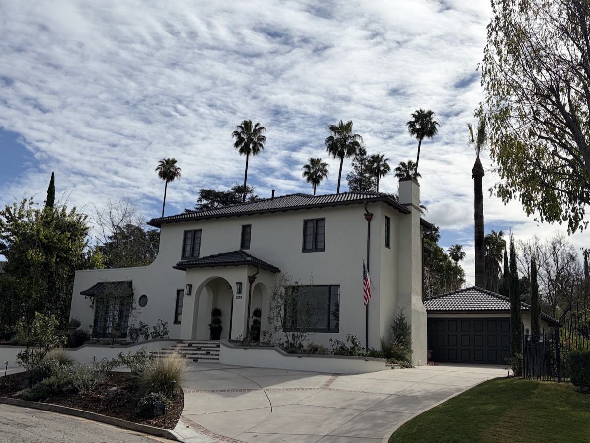 A white two-story Spanish revival house with a low-pitched tile roof, framed by tall palm trees.