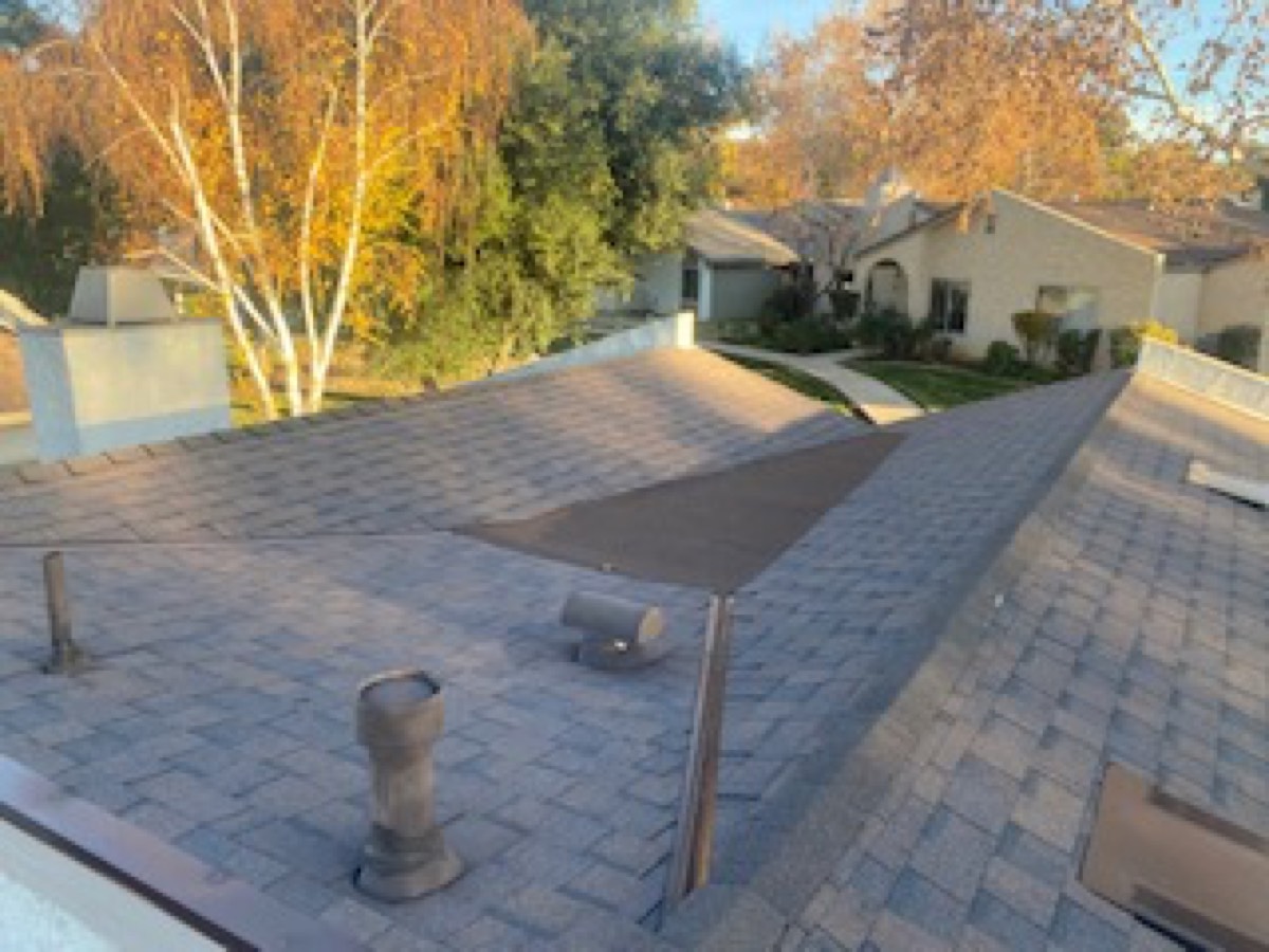 A finished composition roof deck seen from above, with new pipe flashing, a turbine curb, and clean ridge lines.
