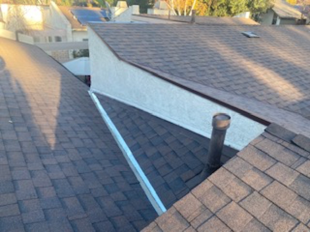A close view of a roof valley with new metal flashing running against a stucco wall.
