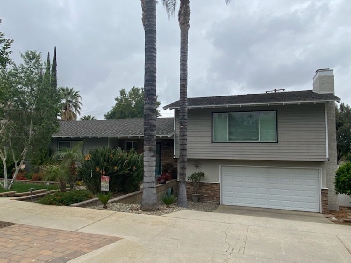 A split-level house with a wide low roof and a two-car garage, palms in the front yard.