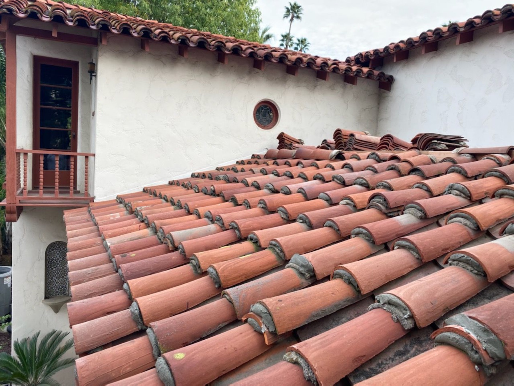 Two-piece clay barrel tile laid across a Spanish revival roof, with the white stucco wall and balcony of the house behind it.
