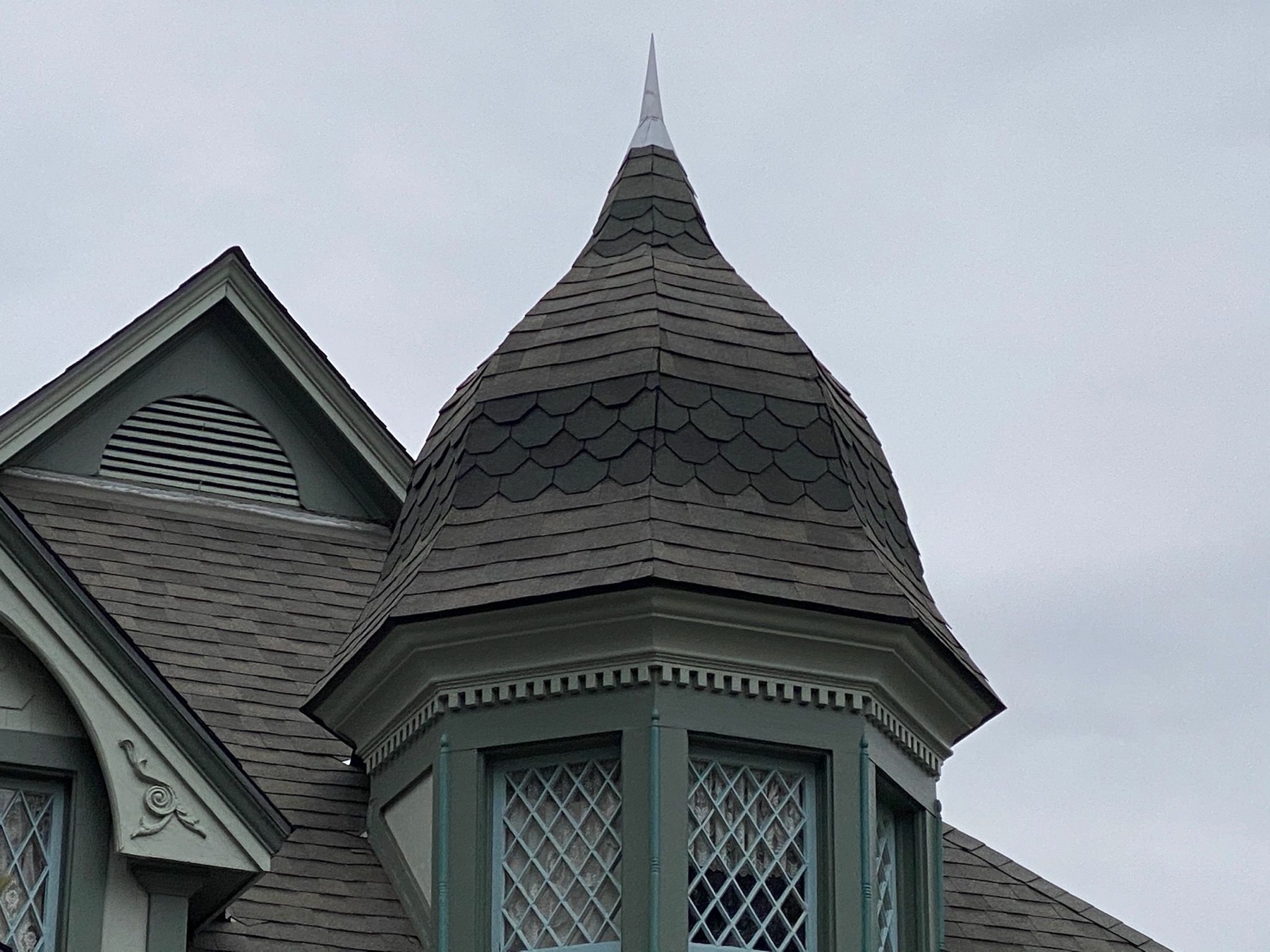 A Victorian turret roofed in scalloped wood shake, rising to a finial above leaded glass windows.